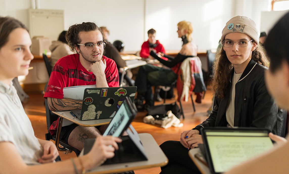 PNCA undergrad students sit at desks in a circle in a classroom, laptops in front of them